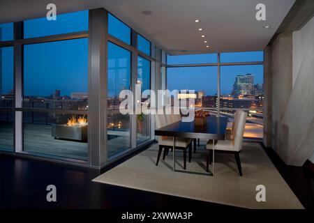 Moderna zona pranzo con finestre a tutta altezza con vista sulla città di notte Foto Stock