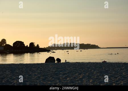 Mentre il sole tramonta sulla spiaggia di Ladeira, i visitatori sfruttano al meglio i raggi d'oro finali della giornata. Il caldo bagliore del sole della sera proietta lunghe ombre sul Foto Stock