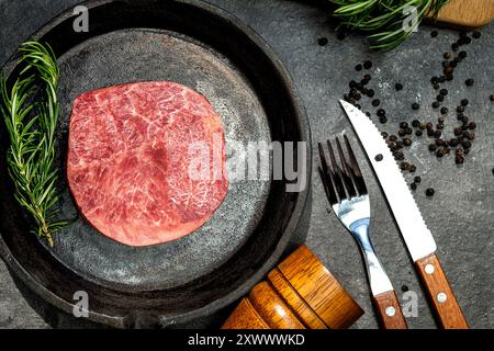 Un pezzo di filetto di carne è su una padella con una forchetta e un coltello accanto ad essa. La carne di filetto è cruda e ha molto condimento Foto Stock