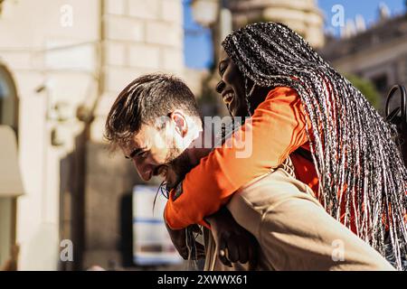 Fidanzato e fidanzata si abbracciano mentre l'uomo porta la donna sulla schiena - coppia multietnica di giovani amanti che si divertono pigg Foto Stock