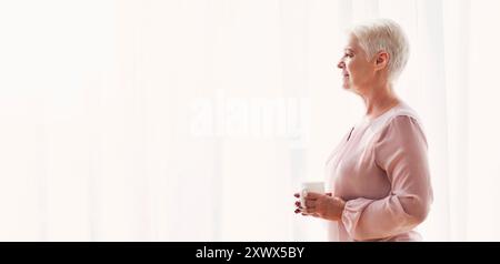 Malinconici senior lady con la tazza di stare accanto alla finestra Foto Stock