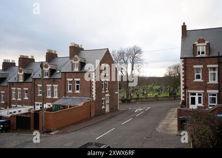 Vista delle case a schiera su Chesterfield Rd a Elswick, Newcastle upon Tyne, con un cimitero visibile sullo sfondo. La giustapposizione di case e tombe evoca temi di comunità e mortalità. Foto Stock