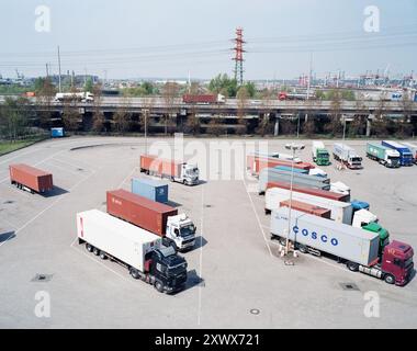 Vista dall'alto dei camion parcheggiati con container presso la stazione Zollabfertigungsstation di Altenwerder, Amburgo. L'immagine simboleggia il coordinamento logistico, il commercio globale e i trasporti efficienti. Foto Stock