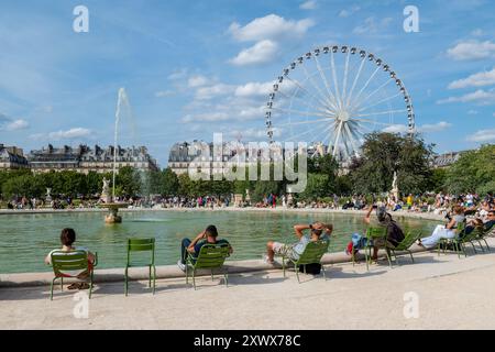 Parigi (Francia): Turisti che si godono il sole in estate al Giardino delle Tuileries. Turisti e parigini seduti su sedie nel parco, intorno a un grande giro Foto Stock