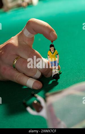 Primo piano di una mano che tiene la prima figura femminile di Tipp-Kick durante una sessione di allenamento di Tipp-Kick a Berlino-Schöneberg. La mano è bendata, a indicare una pratica intensa. Il gioco da tavolo prevede un'elevata concentrazione e abilità. Foto Stock