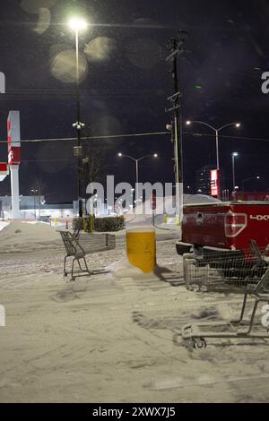 Scena invernale notturna con parcheggio coperto di neve ad Anchorage, Alaska. I carrelli della spesa abbandonati e un pick-up evocano sentimenti di solitudine e abbandono in condizioni fredde e difficili. Foto Stock