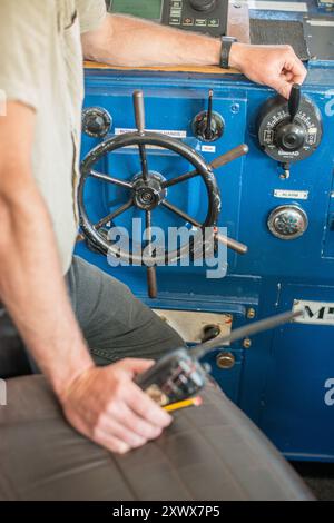 Questa immagine cattura un capitano di nave al timone di una nave marittima, mostrando i sistemi di controllo e le attrezzature. L'attenzione è rivolta ai dettagli intricati della navigazione e alla responsabilità della gestione di una nave. Foto Stock