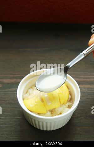 Cucchiaio che aggiunge latte di cocco in un delizioso riso tailandese appiccicoso con Durian chiamato Kao Niaow Turian Foto Stock