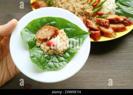 Un boccone di Sai Krok-Planaem, salsicce di maiale alla griglia in stile tailandese con pesce grattugiato e maiale avvolto in una foglia fresca di Betel selvatico Foto Stock