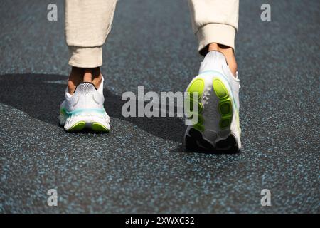 Gambe atlete in sneakers bianche con stativo in ombra sul parco giochi blu all'aperto. Vista posteriore. Allenamento. Primo piano. All'aperto. Foto Stock