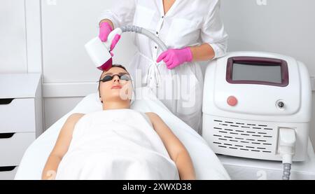 Procedura di epilazione Elos sul viso di una donna. Estetista che fa ringiovanimento laser sulla fronte in un salone di bellezza. Cura della pelle del viso. Foto Stock