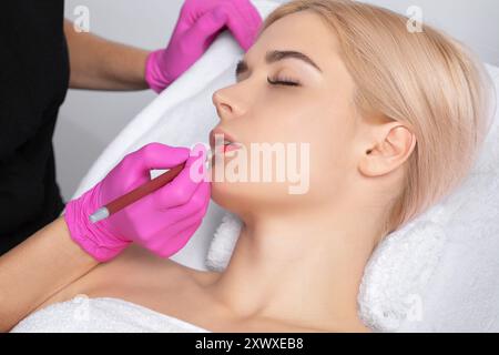 Trucco permanente per le labbra rosse di una bella donna nel salone di bellezza. Primo piano estetista che fa le labbra tatuate. Foto Stock