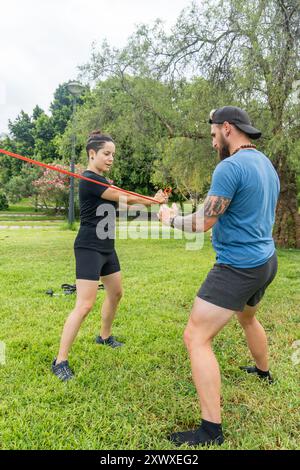 Routine di fitness all'aperto con fasce di resistenza, con due persone focalizzate sull'allenamento di forza in un lussureggiante parco verde. Foto Stock