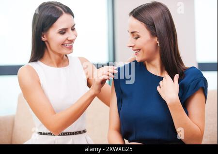 Dovrebbe essere tutto perfetto. Bella giovane donna in abito da sera che aiuta la sua amica a vestirsi mentre entrambe sono sedute sul divano Foto Stock