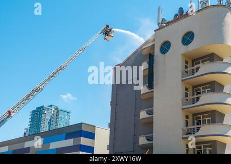 I vigili del fuoco estinguono il fuoco sul tetto della casa utilizzando una scala estesa dotata di tubo flessibile per spruzzare acqua sul tetto dell'edificio con fumo Foto Stock