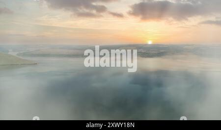 L'alba è nebbiosa su un lago calmo con dolci colline sullo sfondo. Sfondo spazio fotocopie per vista aerea. Concetto di ottimismo ecologico. Bellezza della natura. Foto Stock