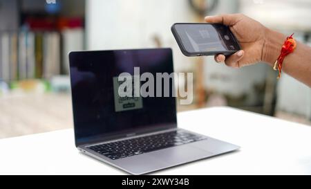 Giovane indiano che paga le bollette con il cellulare e il portatile. Scansione codice QR e concetto di pagamento. Lavora da casa Foto Stock