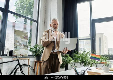 Un uomo barbuto di mezza età con una tuta insegna online, guardando attentamente il suo notebook. Foto Stock