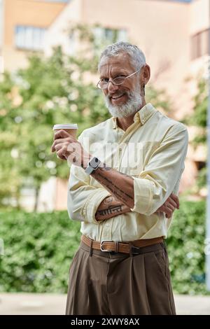 Un uomo maturo con la barba sta fuori, sorridendo mentre tiene una tazza di caffè. Foto Stock