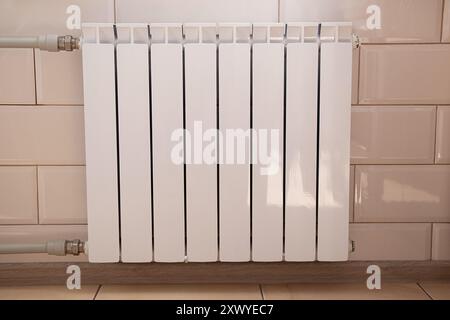 Radiatore bianco nell'appartamento sulla parete con piastrelle bianche in cucina sotto la finestra, riscaldamento centralizzato, casa calda Foto Stock