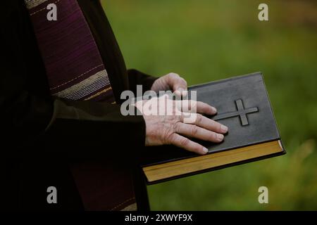 Primo piano medio della bibbia di cuoio nero nelle mani dei vecchi sacerdoti Foto Stock