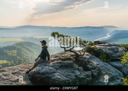 Un uomo seduto su una roccia, ad ammirare il tramonto sulle montagne. Svizzera sassone, Germania Foto Stock