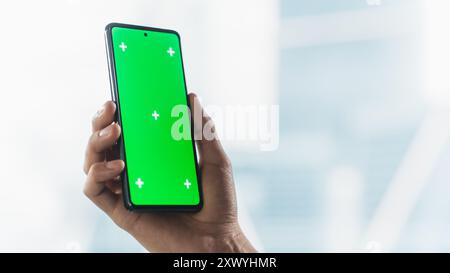 Persona aziendale anonima che utilizza uno smartphone con schermo di mascheratura verde per la pubblicazione sui social media. Mano dell'uomo che tiene il cellulare in verticale con area isolata per app, software, promozione sito Web Foto Stock