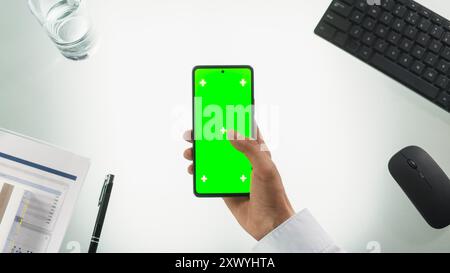 Persona anonima che utilizza uno smartphone con display Chromakey con schermo verde di occultamento con segnaposto Motion Tracker. Manager che naviga in linea, scorri e tocca sul telefono. Vista dall'alto verso il basso Foto Stock