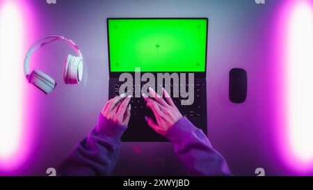 Foto dall'alto di una sviluppatrice software donna che lavora su un notebook in una stanza elegante con luci al neon. Computer con modello chiave Chroma Green Screen per servizi di marketing digitale, applicazioni, software Foto Stock