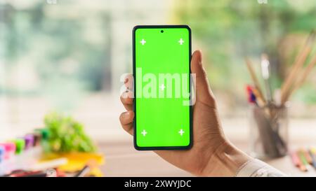 Vista POV di un progettista con smartphone con schermo verde. Vista in prima persona di un uomo che detiene un dispositivo con area isolata per app, software, promozione sito Web Foto Stock