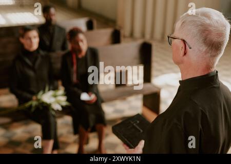 Vista a spalla del prete dai capelli d'argento che prega e tiene la Bibbia Foto Stock