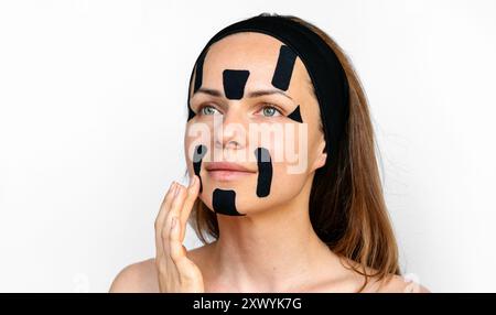 La modella di bellezza della giovane donna applica nastri facciali neri sul suo viso. Foto Stock