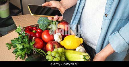 Ordine online di cibo sano biologico coltivato da fattoria. Donna che disimballa il cartone con verdure e frutta. Foto Stock