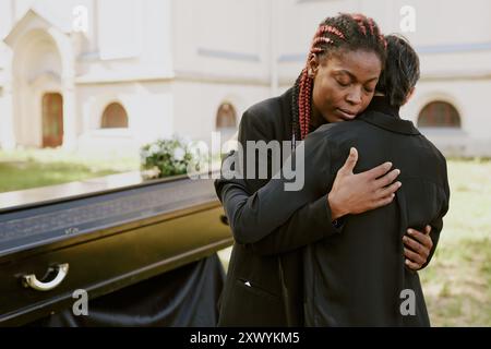 Donna afroamericana che abbraccia la sua mamma caucasica e piange al funerale Foto Stock