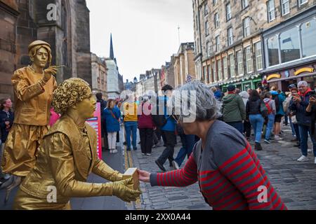 Edinburgh Festival Fringe, Royal Mile, Scotland, UK 21 agosto 2024. Mercoledì della terza settimana sul miglio, un po' meno occupato e il pubblico più piccolo di prima. Il tempo era molto ventoso, con incantesimi assolati e docce. Nella foto: Statue di strada viventi in oro e gloria che si esibiscono nelle alcove Royal Mile, Edinburgh Festival Fringe, Scozia, 2024. Uno dei tanti costumi di Izabella Lutrek con David French. Credito: Arch White/alamy notizie dal vivo. Foto Stock