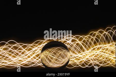 Una fotografia a lunga esposizione. Fotografia di pittura di luce - vorticose onde di luce al neon dietro una lente a sfera di vetro. Foto Stock