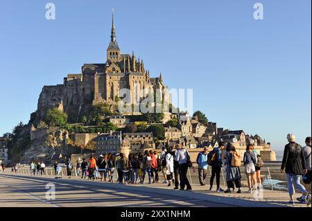 I turisti camminano sulla nuova passerella verso Mont-Saint-Michel, sito patrimonio dell'umanità dell'UNESCO, dipartimento della Manche, regione della Normandia, Francia, Europa Foto Stock