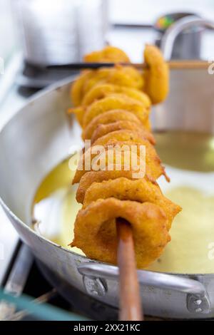 Uno spiedino di picaroni fritti viene cotto in una padella. L'impasto è dorato e sembra delizioso Foto Stock