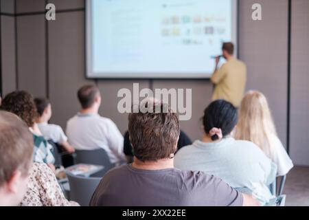 Gruppo di persone che partecipano a un seminario formativo incentrato sul relatore che presenta contenuti digitali sullo schermo Foto Stock