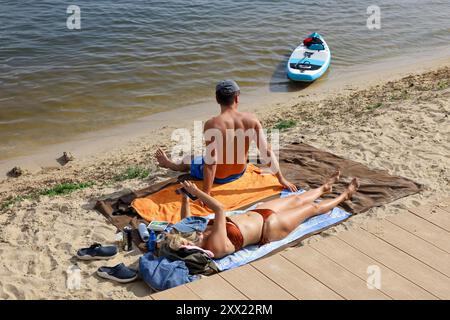 Coppia che prendeva il sole sulla spiaggia del fiume. Tempo caldo, picnic estivo Foto Stock