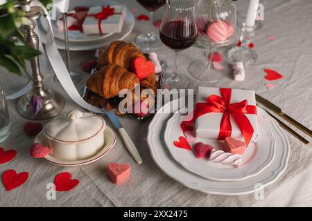 Primo piano di un romantico tavolo per due con confezioni regalo, caramelle, croissant e vino rosso Foto Stock
