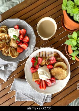 Vista dall'alto di pancake, fragole fresche, panna montata e burro di arachidi con una tazza di caffè su un tavolo Foto Stock