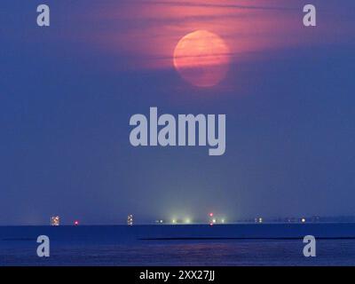 Warden Bay, Kent, Regno Unito. 21 agosto 2024. Meteo nel Regno Unito: La superluna di storione blu che si affievolisce sopra la costa del Kent vista da Warden Bay, Kent. Fig.: Il blocco torre Arlington House a Margate può essere visto in basso a sinistra. Crediti: James Bell/Alamy Live News Foto Stock