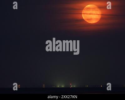 Warden Bay, Kent, Regno Unito. 21 agosto 2024. Meteo nel Regno Unito: La superluna di storione blu che si affievolisce sopra la costa del Kent vista da Warden Bay, Kent. Fig.: tower block Arlington House a Margate in basso a sinistra dell'orizzonte. Crediti: James Bell/Alamy Live News Foto Stock