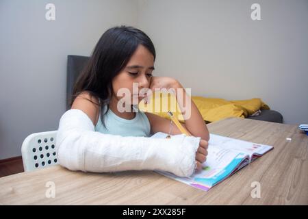 Una bambina con un braccio rotto studia nella sua stanza Foto Stock