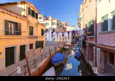 Uno stretto canale veneziano con barche e lavanderia appesi tra gli edifici di Venezia, Italia Foto Stock