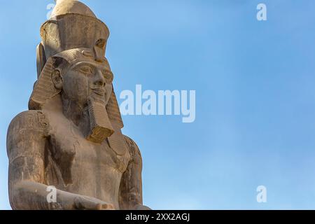 La colossale statua di Ramsete II domina il tempio di Luxor, testimonianza del potere del faraone e della grandezza dell'antica Tebe. Foto Stock