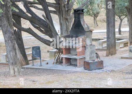 Vecchio barbecue in pietra con camino in un'area di riposo del parco pubblico con nessuno in giro in una giornata di sole Foto Stock