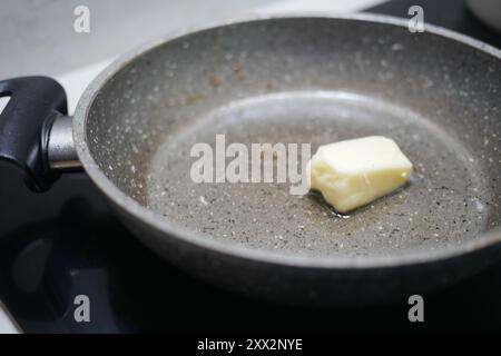 Un pezzo di burro che si scioglie piacevolmente in una padella antiaderente presso la postazione di cottura Foto Stock