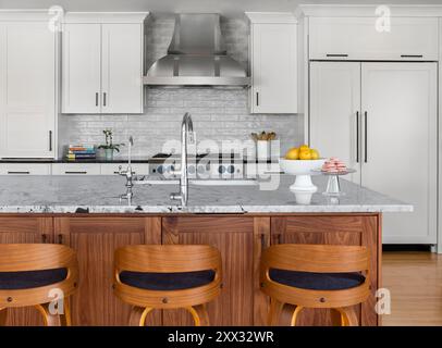 Cucina con armadi bianchi e noci e sgabelli moderni sull'isola Foto Stock